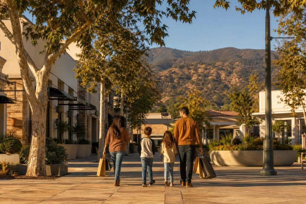 Family walking through Granada Hills Town Center plaza with mature trees, retail storefronts, and San Fernando Valley hillsides visible in afternoon